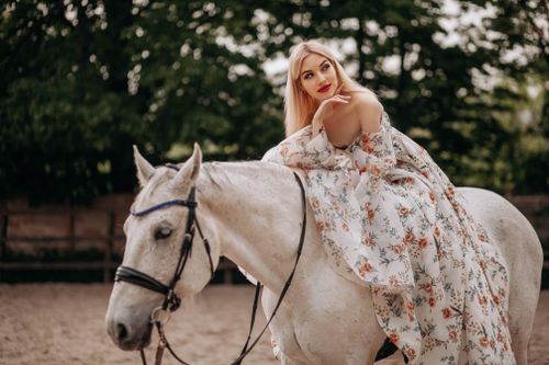 Free A woman in a floral dress gracefully sits on a white horse in an outdoor setting. Stock Photo