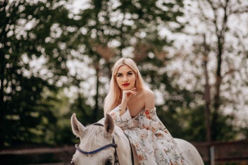 Free A fashionable woman in a floral dress sits elegantly on a horse surrounded by nature. Stock Photo