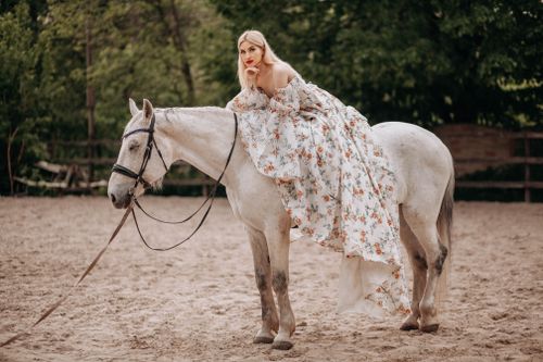 Free Elegant woman in a floral dress on a white horse in a sandy paddock Stock Photo