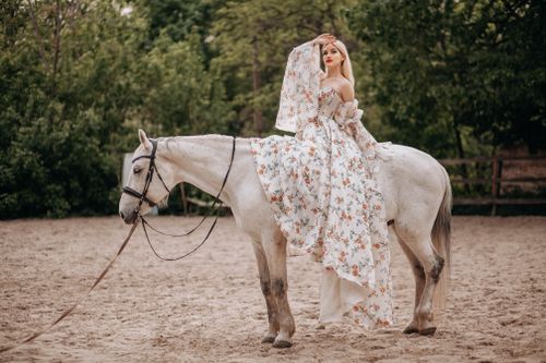 Free A woman in a floral dress riding a white horse in an outdoor arena. Stock Photo