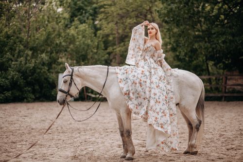 Free A woman in a floral dress gracefully sits atop a white horse outdoors. Stock Photo