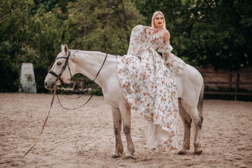 Free A stylish woman in a floral dress seated elegantly on a white horse outdoors. Stock Photo
