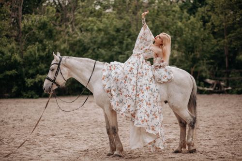 Free Woman in floral dress gracefully poses on a horse in an outdoor setting. Stock Photo