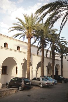 Charming Mediterranean building with palm trees and vintage cars parked outside, ideal for travel and architecture themes.