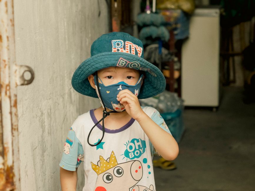 Young boy indoors wearing a hat and mask, embracing modern urban style.