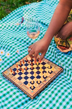 A close-up of a hand playing chess on a vibrant checkered blanket with a glass of wine in Bauru, SP, Brazil.