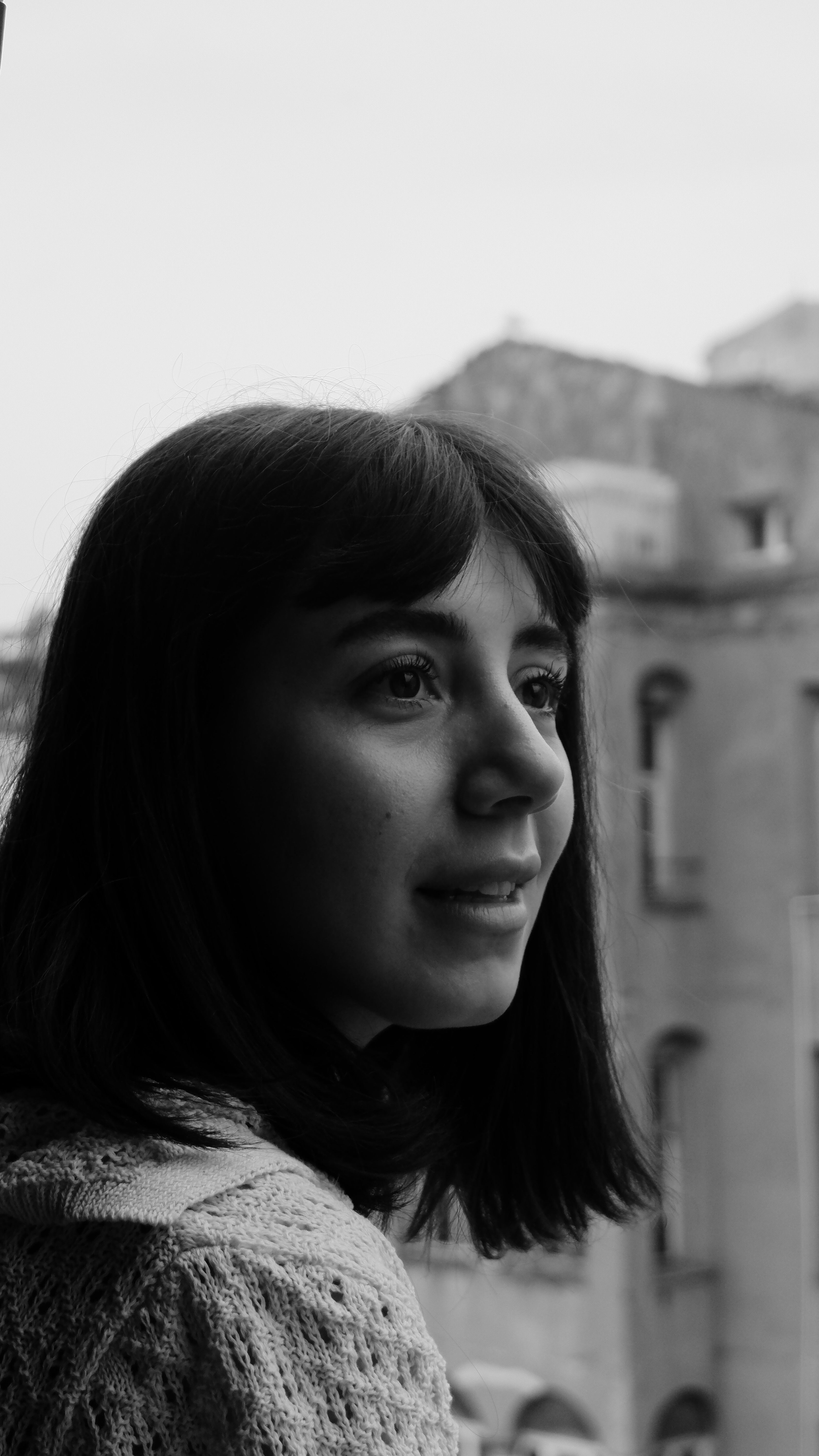 A woman gazes pensively out the window, captured in a black and white portrait highlighting her thoughtful expression.