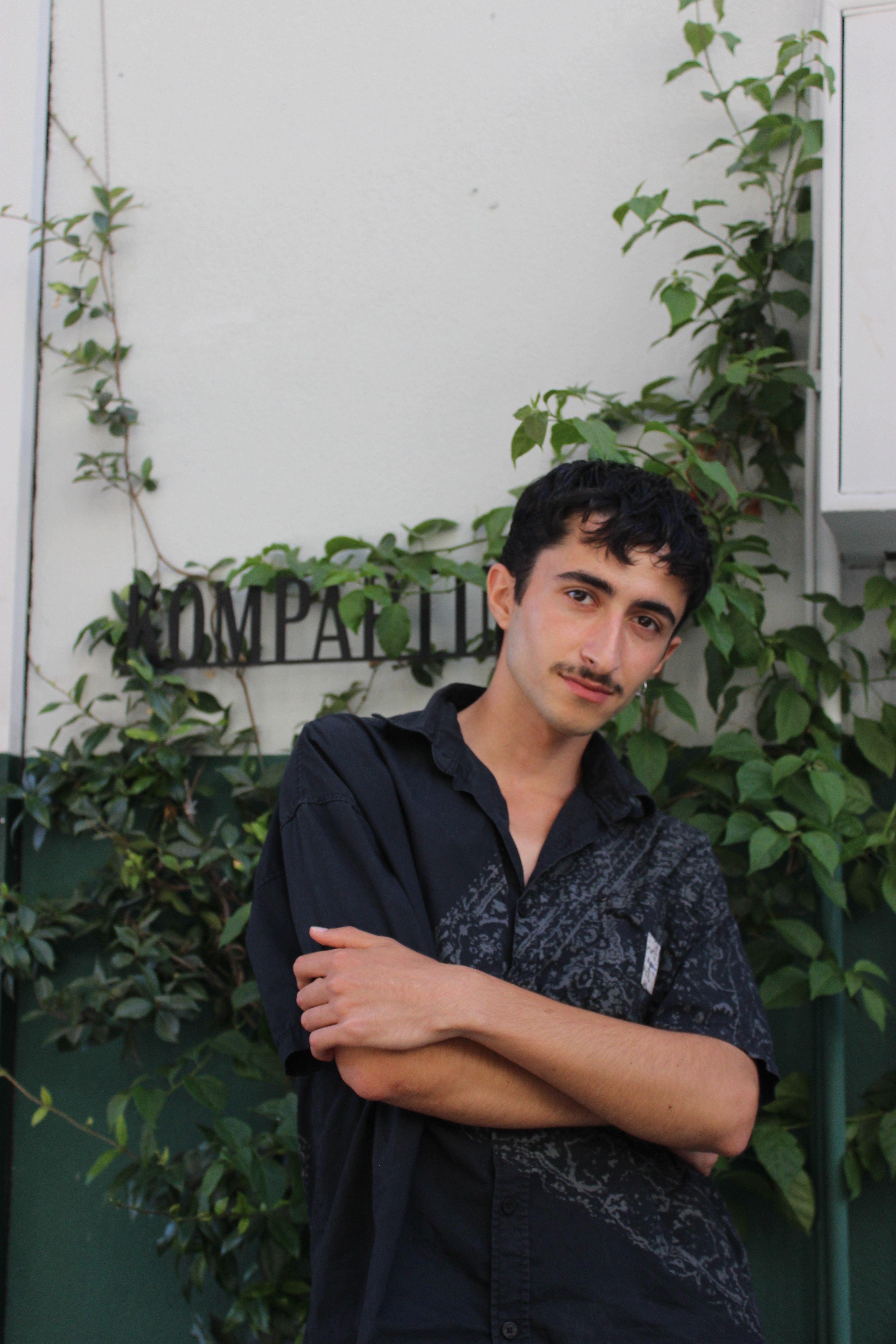 A casual portrait of a young man standing against a leafy backdrop. Ideal for lifestyle themes.