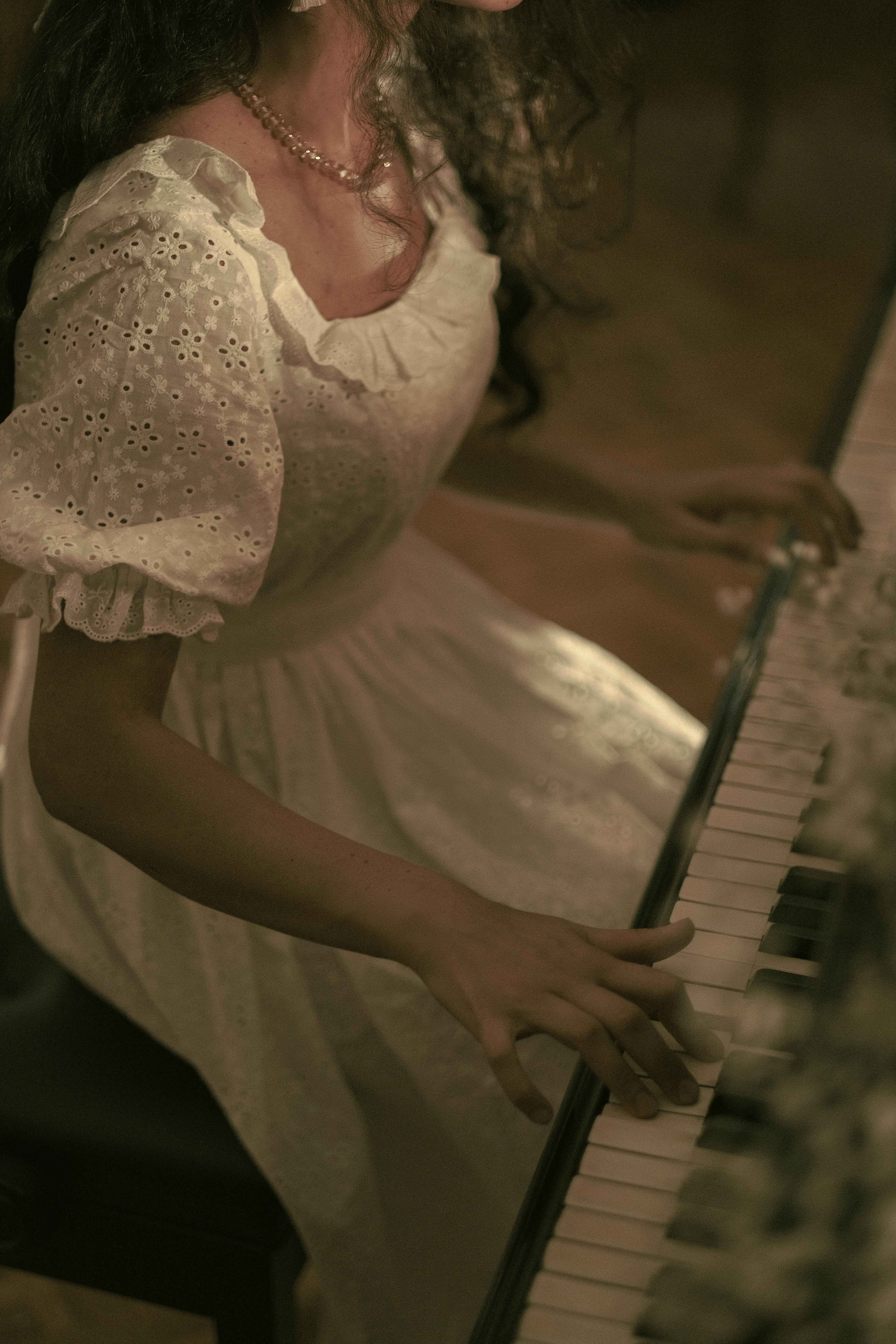 A woman in a vintage dress playing piano, creating a nostalgic and artistic mood indoors.