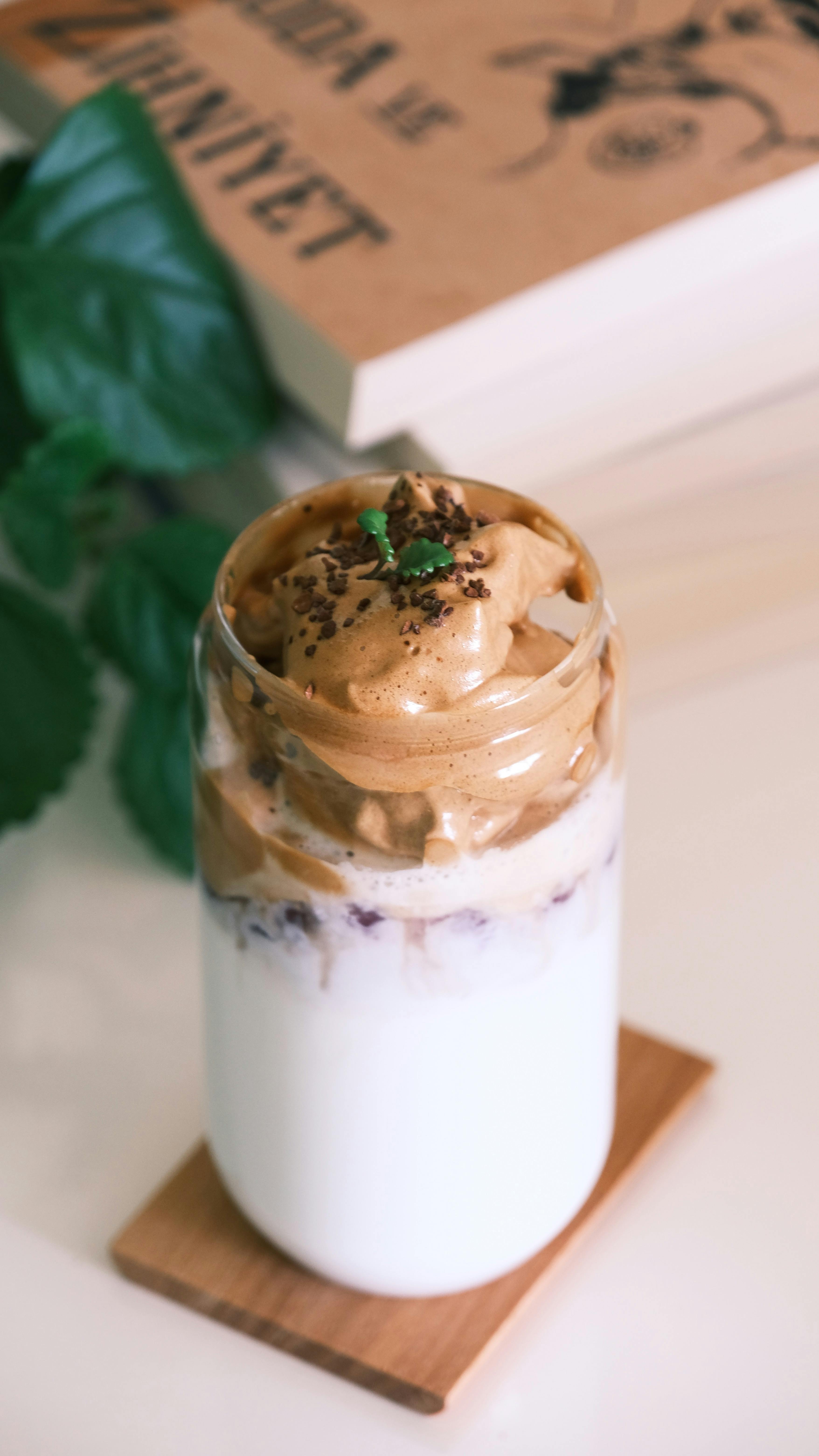 Delicious dalgona coffee with creamy foam served in a glass jar on a table with a book in the background.