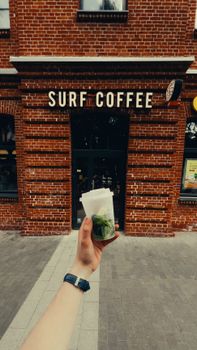 A person holding a drink in front of the Surf Coffee cafe, showcasing rustic red brick architecture.