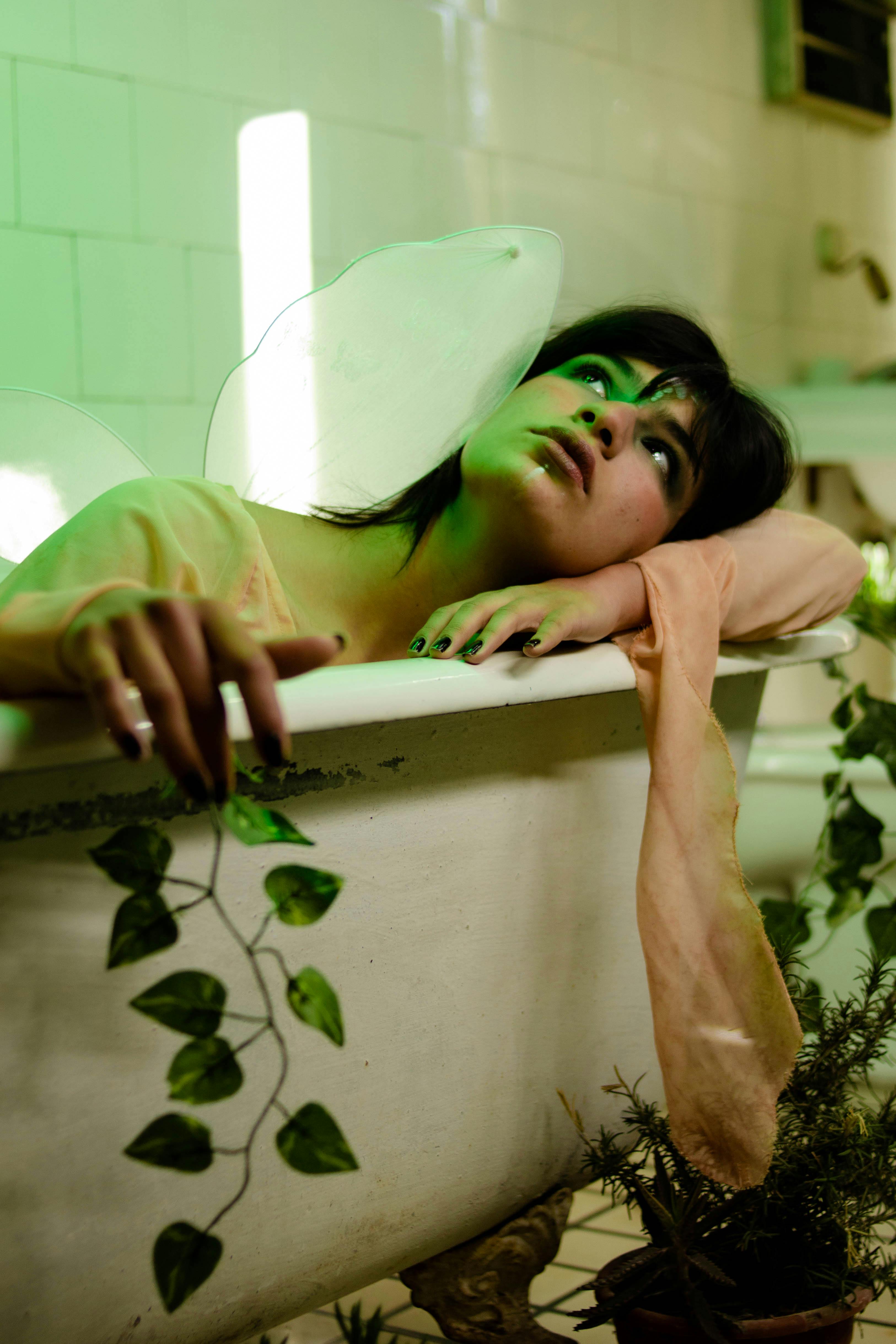 A woman with fairy-like aura indulges in a relaxing bath surrounded by plants indoors.