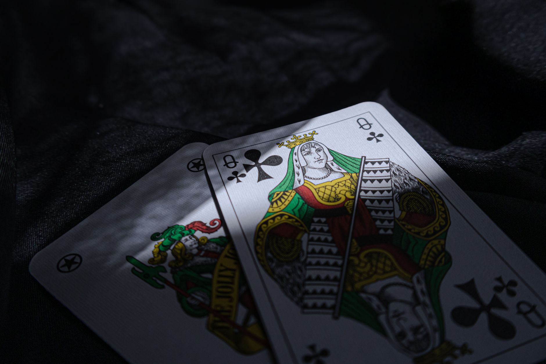 Close-up of queen of clubs playing cards on a dark surface, emphasizing a casino theme.