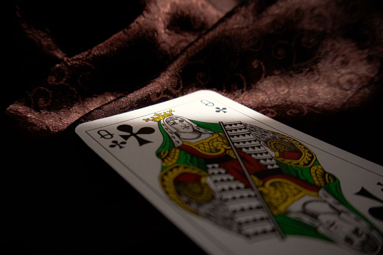 close up of a queen of clubs playing card on a dark velvet fabric high