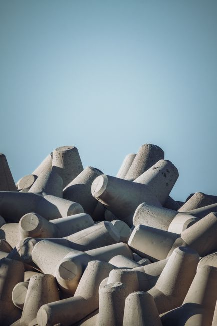 Fotomural Montón de tetrapod de concreto gris apilados al aire libre bajo un cielo azul claro.
