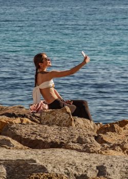Woman taking a selfie on rocky beach in Alicante, enjoying the sea and sun.