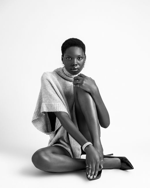 Black and white photo of a stylish black woman sitting in a studio, wearing a sweater.