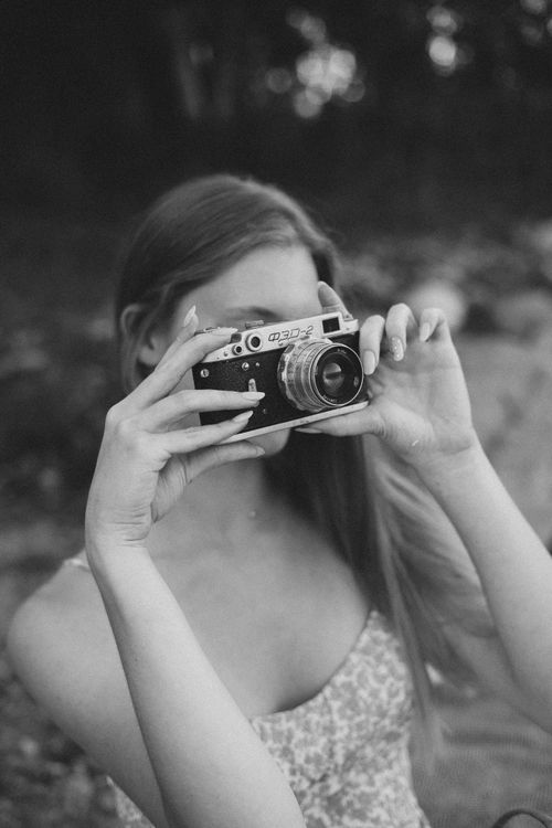 Free Black and white portrait of a woman taking a picture with a film camera, capturing a timeless vintage aesthetic. Stock Photo