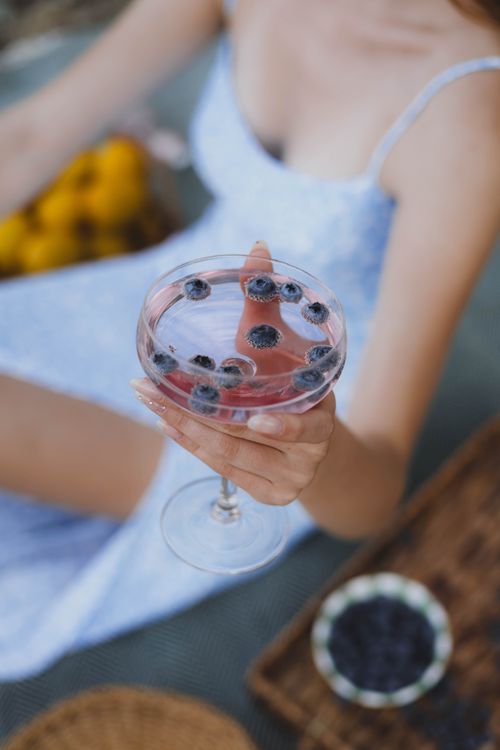 Free Elegant woman holding a blueberry-infused cocktail during a summer picnic. Stock Photo