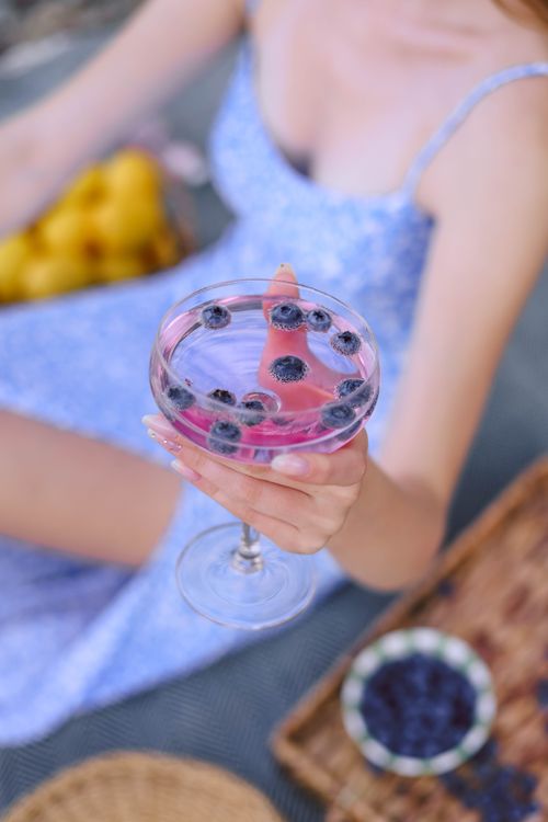 Free Woman holding a refreshing berry cocktail during a vibrant summer picnic. Stock Photo