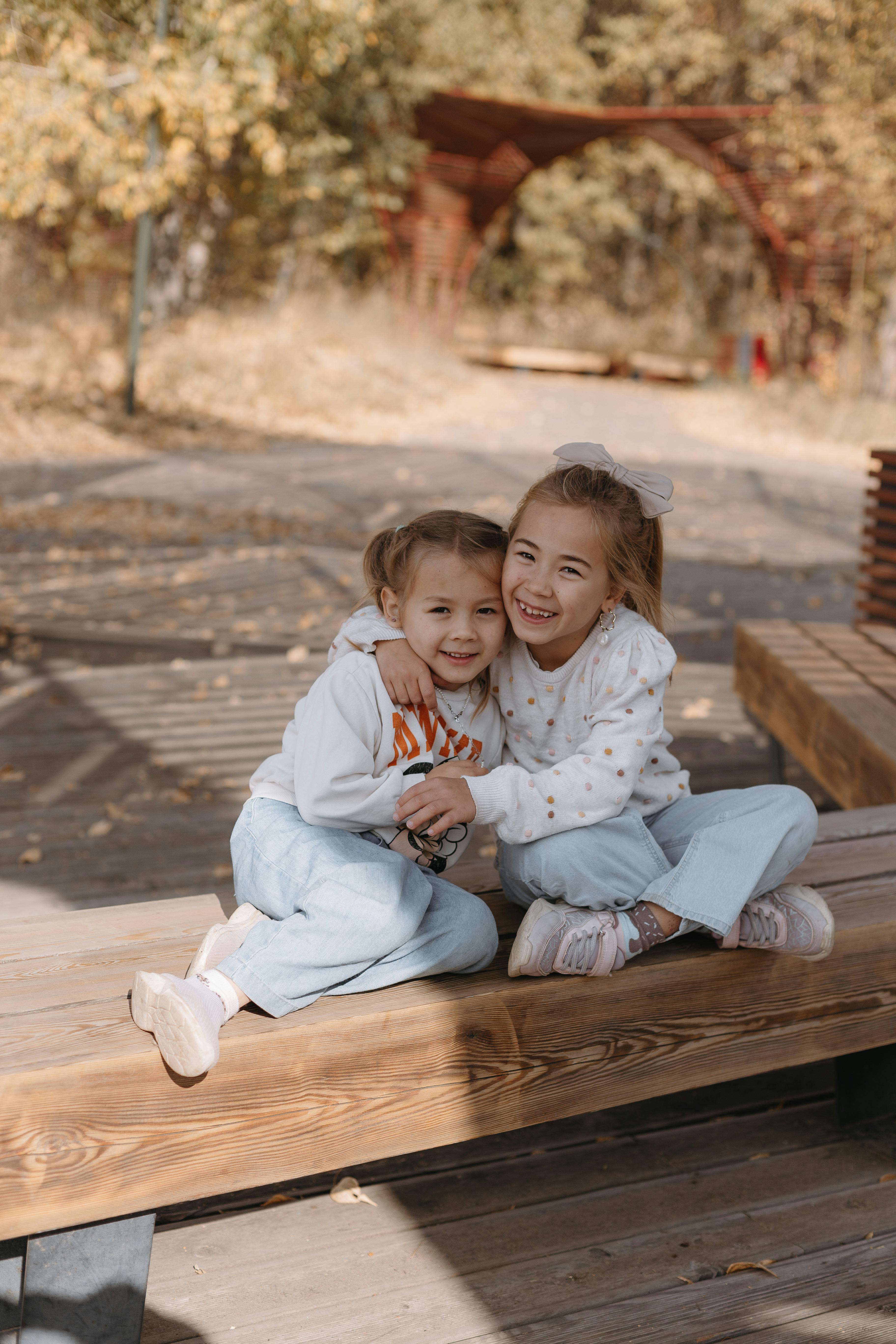 two little girls sitting on a bench in the woods