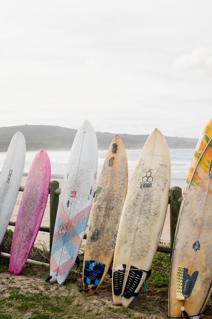 A variety of surfboards lined up on a sandy beach, ready for surf adventures.