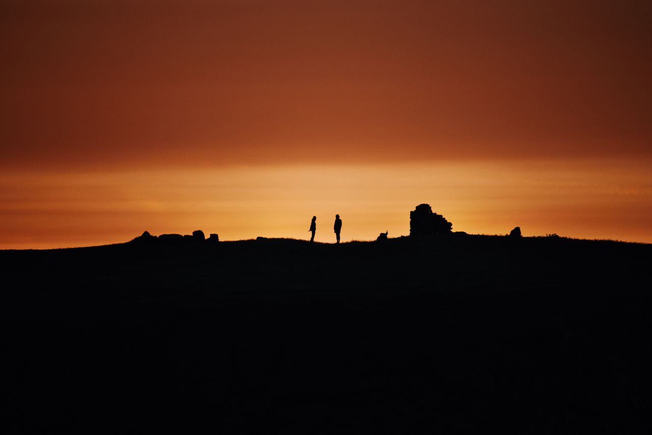 two silhouetted figures stand against a dramatic sunset in crozon bret
