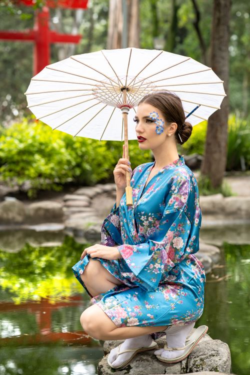Free A woman in a blue floral kimono poses with a traditional umbrella in a serene outdoor setting. Stock Photo
