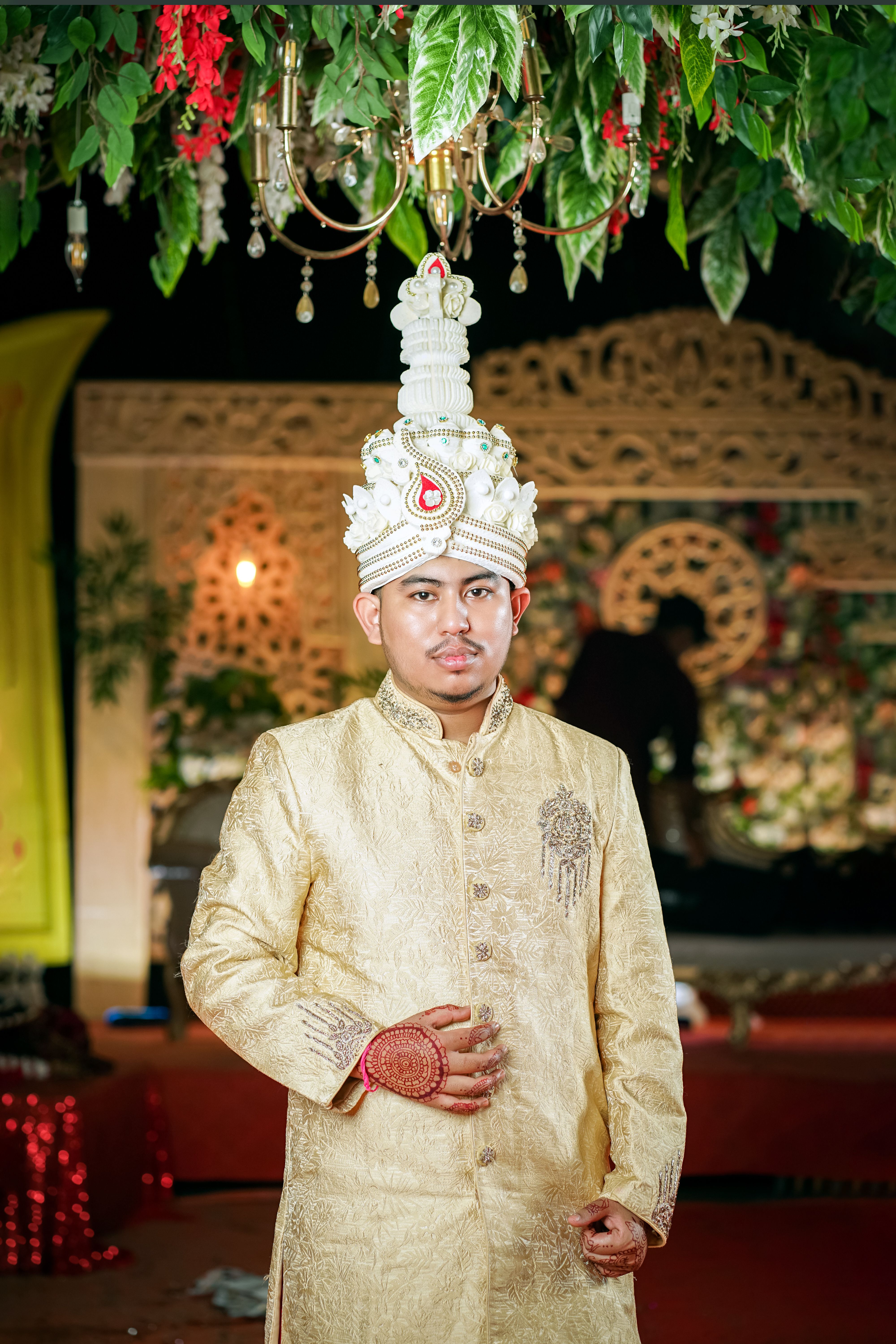 Groom in traditional Indian wedding attire posing under decorative floral canopy.