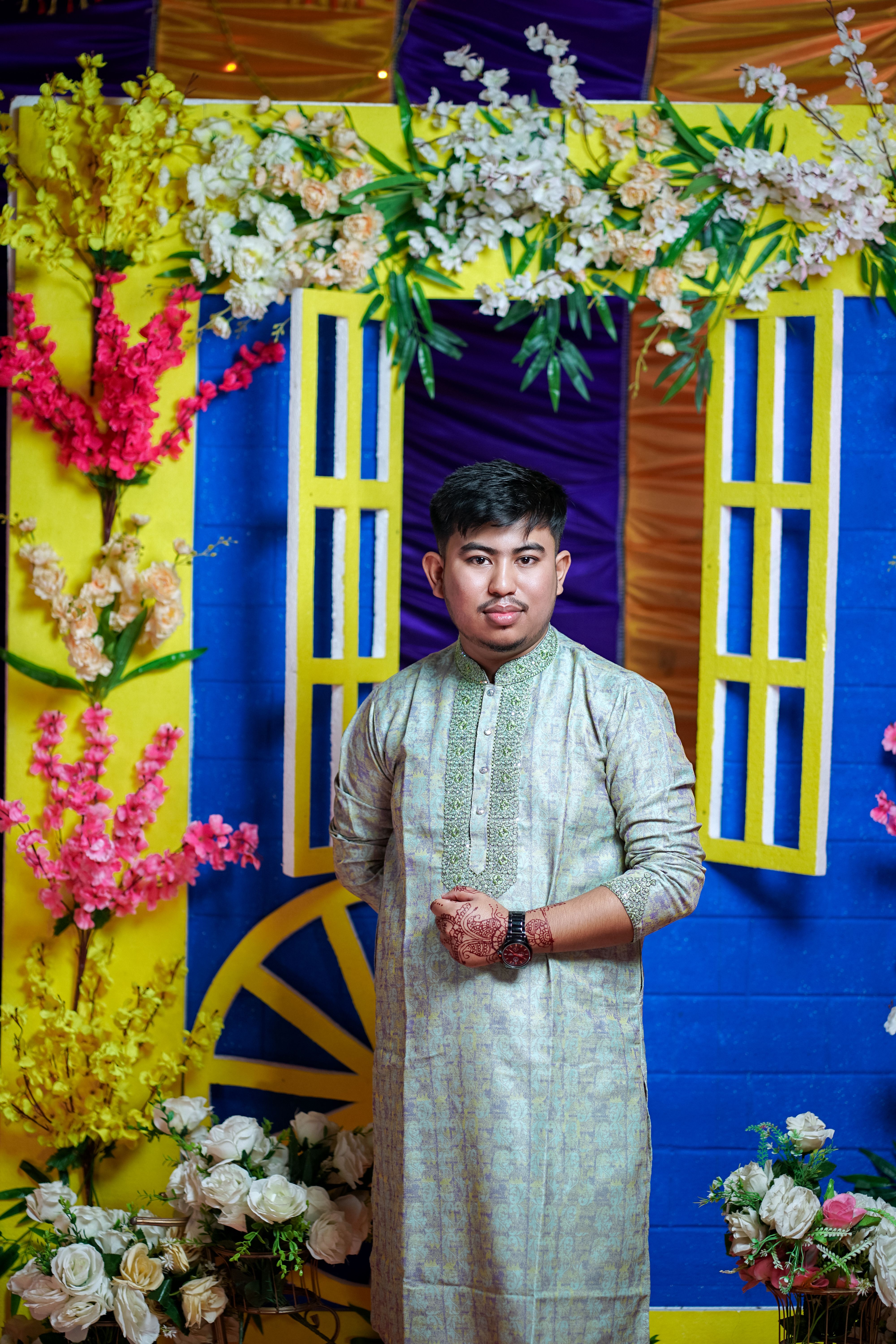 A man in a traditional outfit standing in front of a floral backdrop ...
