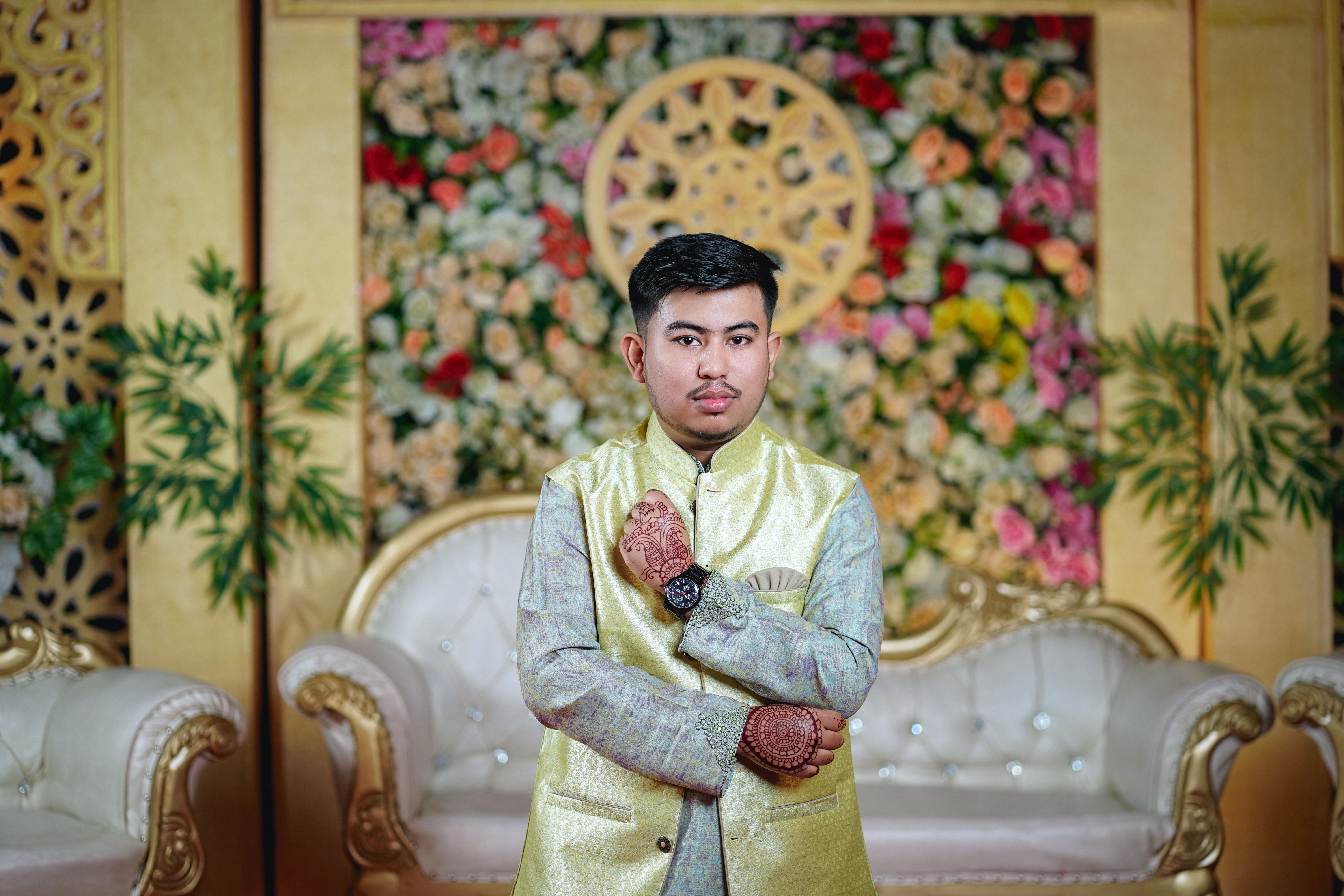 A man in a yellow and gold outfit standing in front of a floral wall ...
