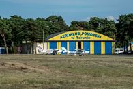 Two small planes parked at Aeroklub Pomorski hangar in Torun, Poland on a sunny day.
