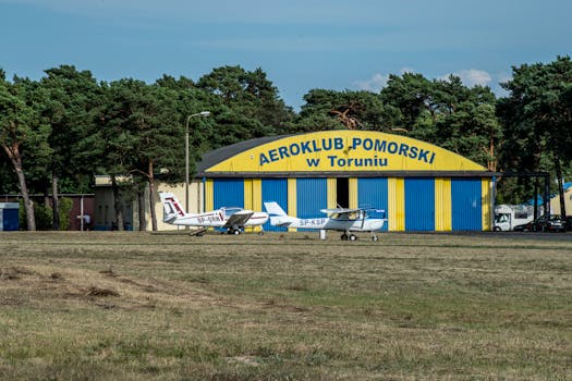 Two small planes parked at Aeroklub Pomorski hangar in Torun, Poland on a sunny day.