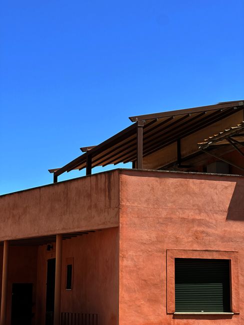 An exterior view of an adobe house with a minimalist modern roof against a clear blue sky.