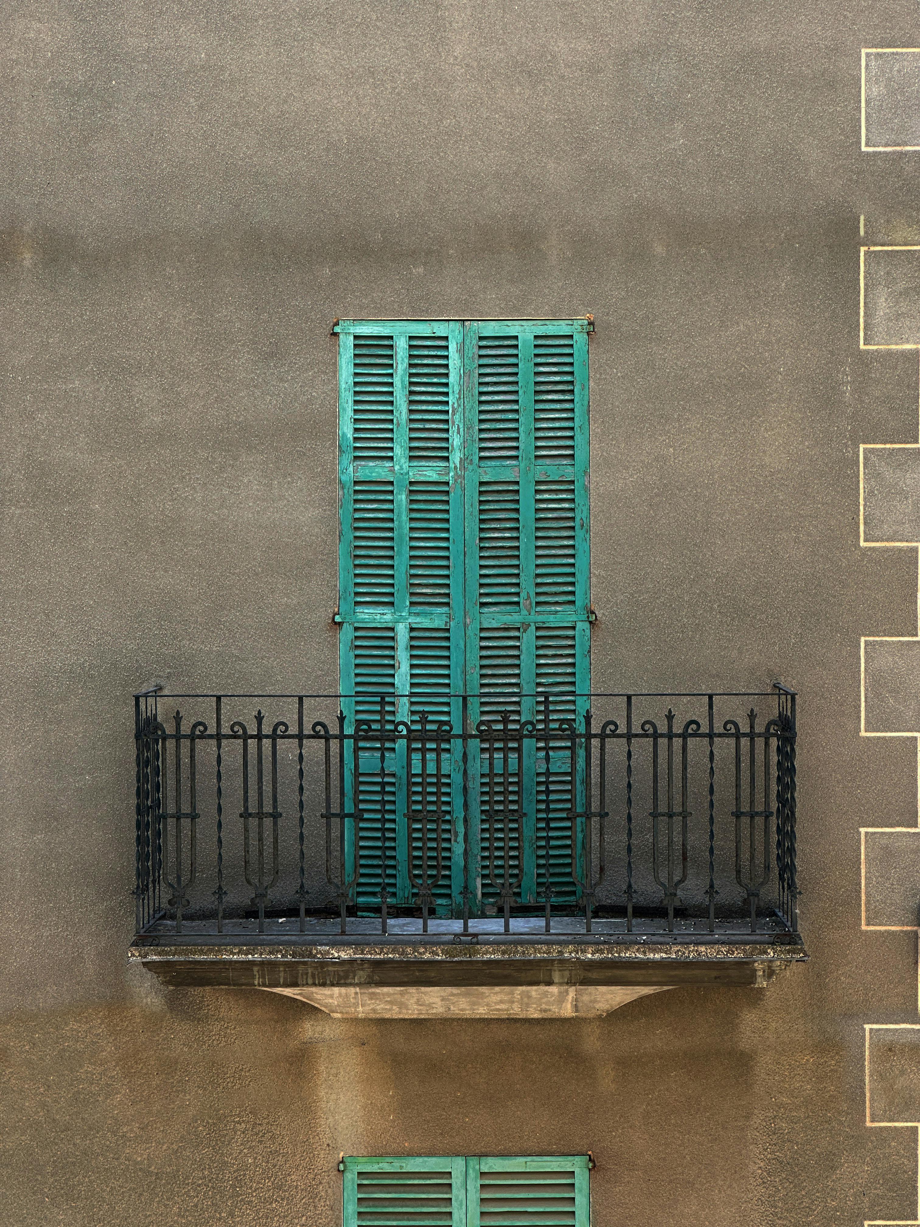 Old balcony with closed green shutters on a textured urban wall.
