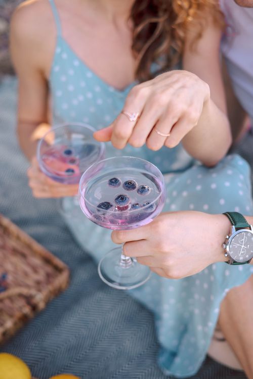 Free Elegant outdoor picnic featuring blueberry-infused mocktails in coupe glasses, set against a summer backdrop. Stock Photo