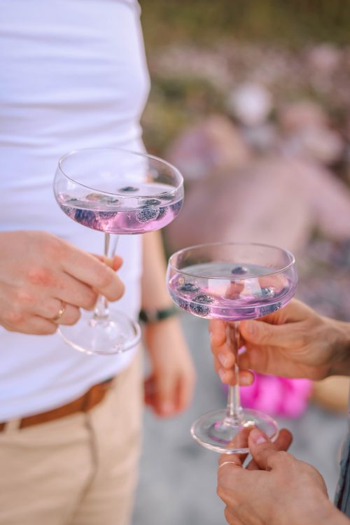 Free Two people clinking glasses filled with pink blueberry cocktails. Perfect for summer celebrations. Stock Photo