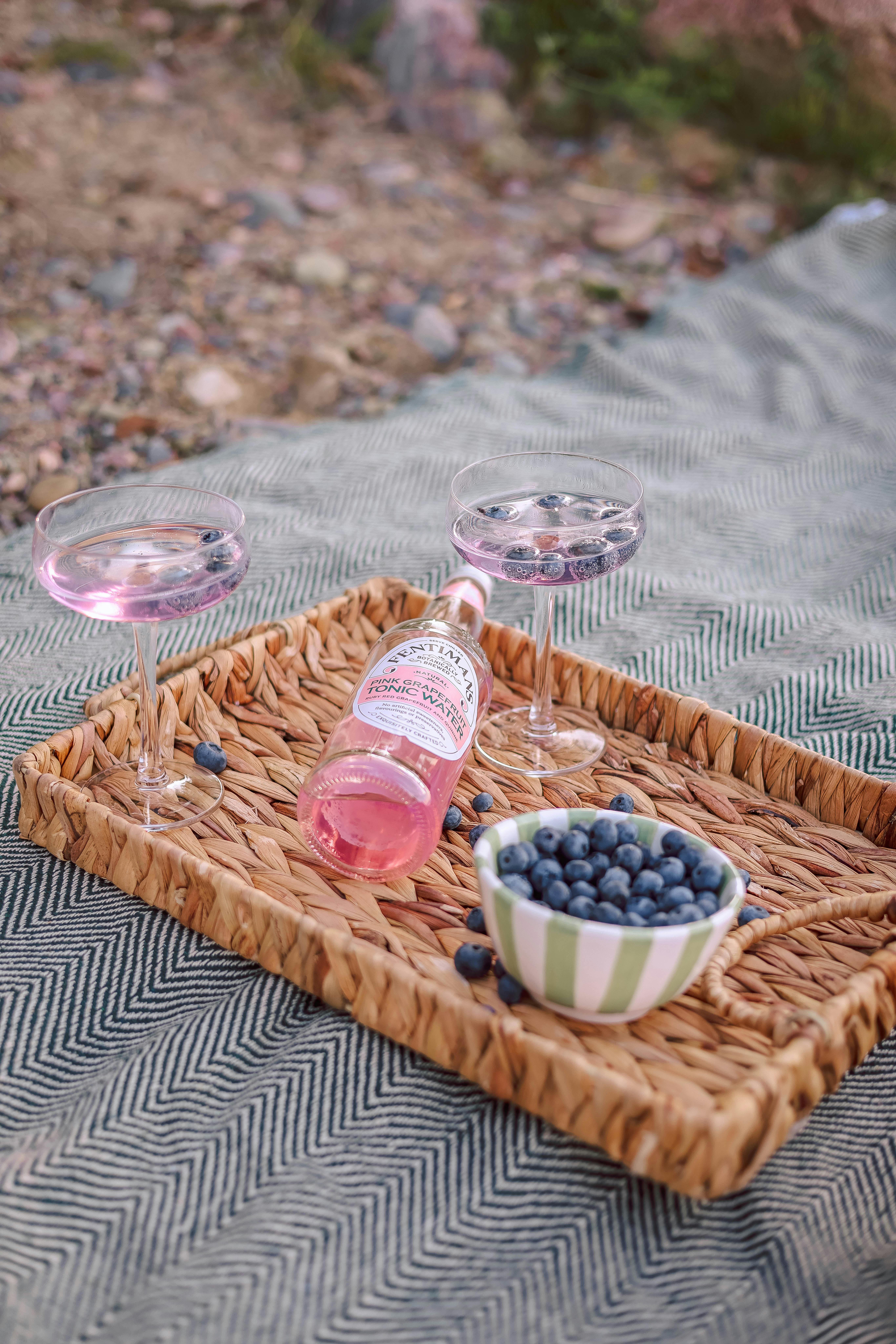 Woven tray holding pink drinks and blueberries for a refreshing outdoor picnic experience.