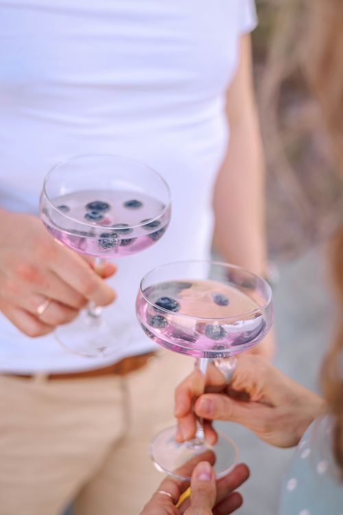 Free Two adults toasting with pink berry cocktails outdoors, embodying summer leisure. Stock Photo
