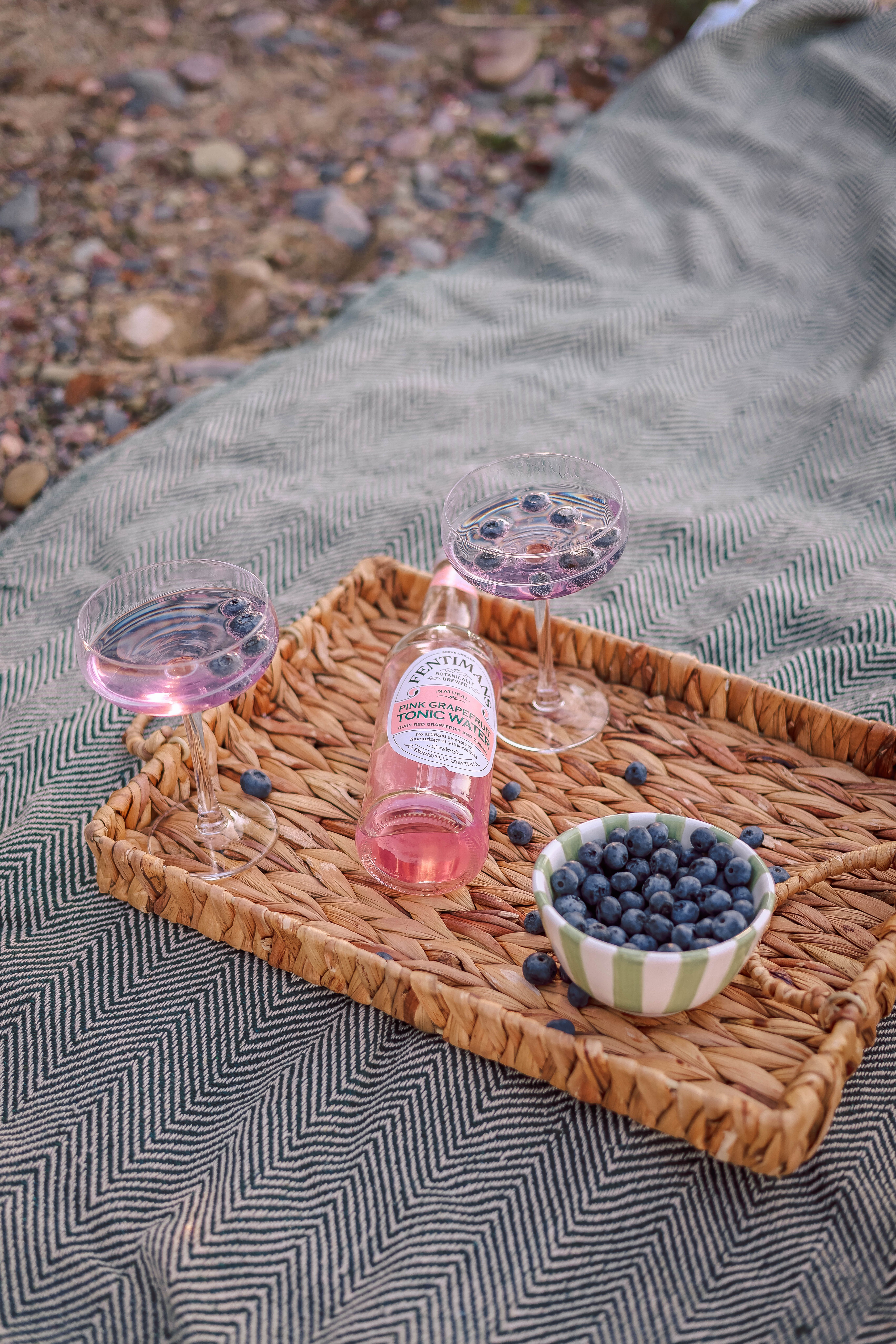 Two glasses of refreshing blueberry drink with a bottle on a picnic blanket, perfect for summer relaxation.