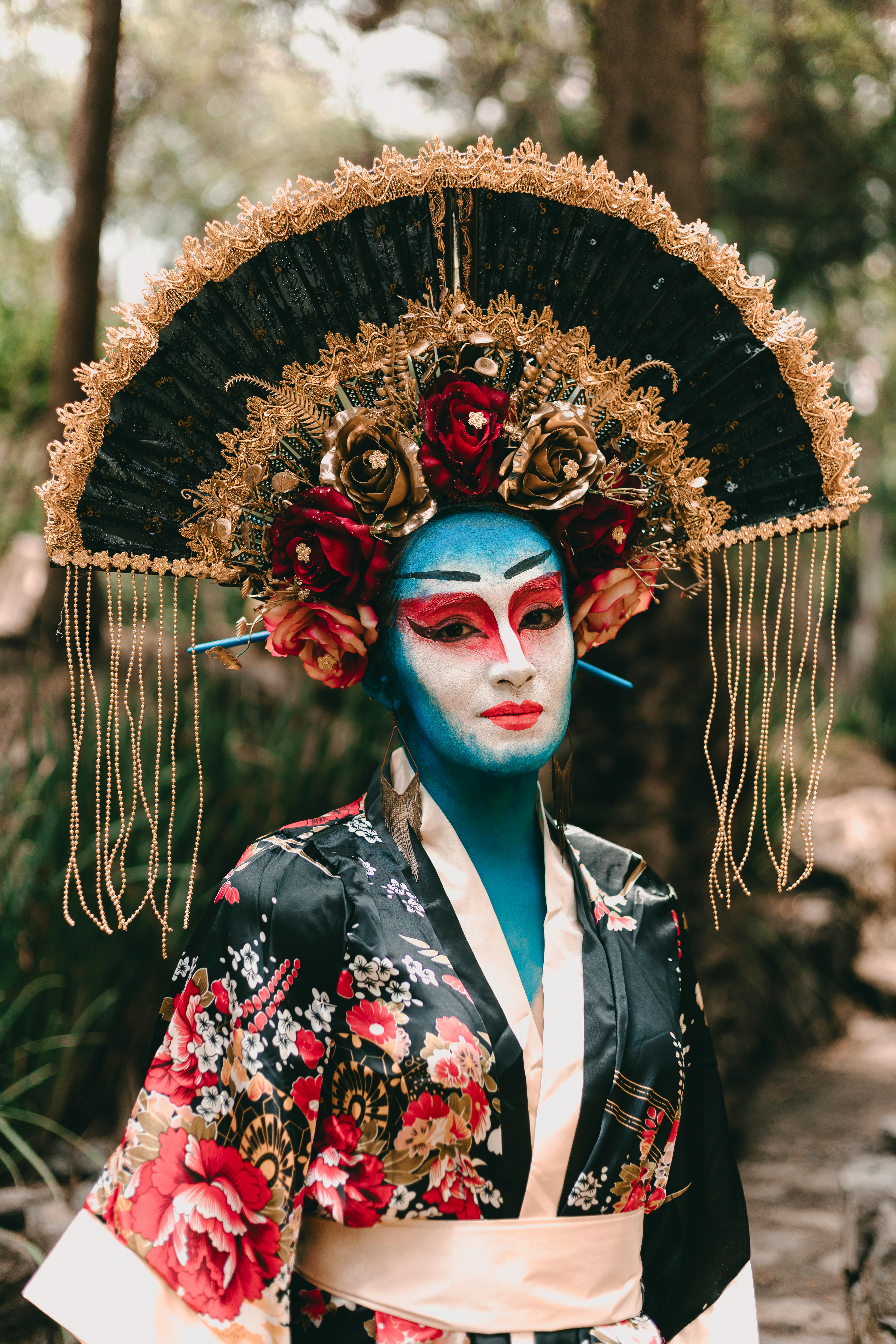 Free A striking portrait of a woman in traditional Japanese attire with elaborate makeup and headpiece, set outdoors. Stock Photo