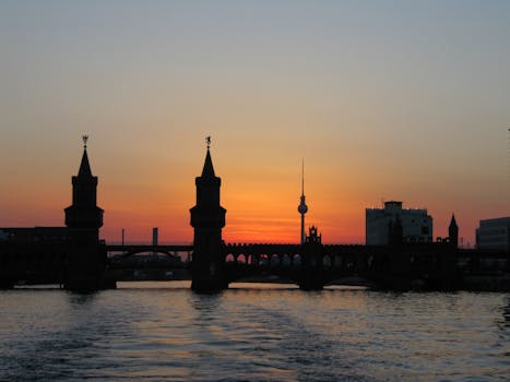 Silhouette of Berlin's Oberbaum Bridge against a stunning sunset sky, reflecting in the Spree River.