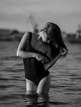 Artistic black and white portrait of a woman in a swimsuit standing in the water. Captured at sunset.