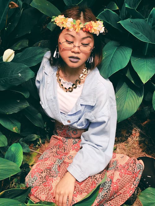 Woman in Eyeglasses, Blue Dress Shirt, and Pink Floral Skirt Sitting on Leaves