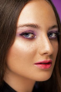 Close-up portrait of a woman featuring colorful makeup with purple eyeshadow and pink lips.