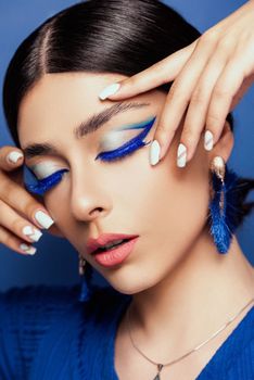 Chic portrait of a woman with striking blue makeup and stylish accessories, eyes closed.
