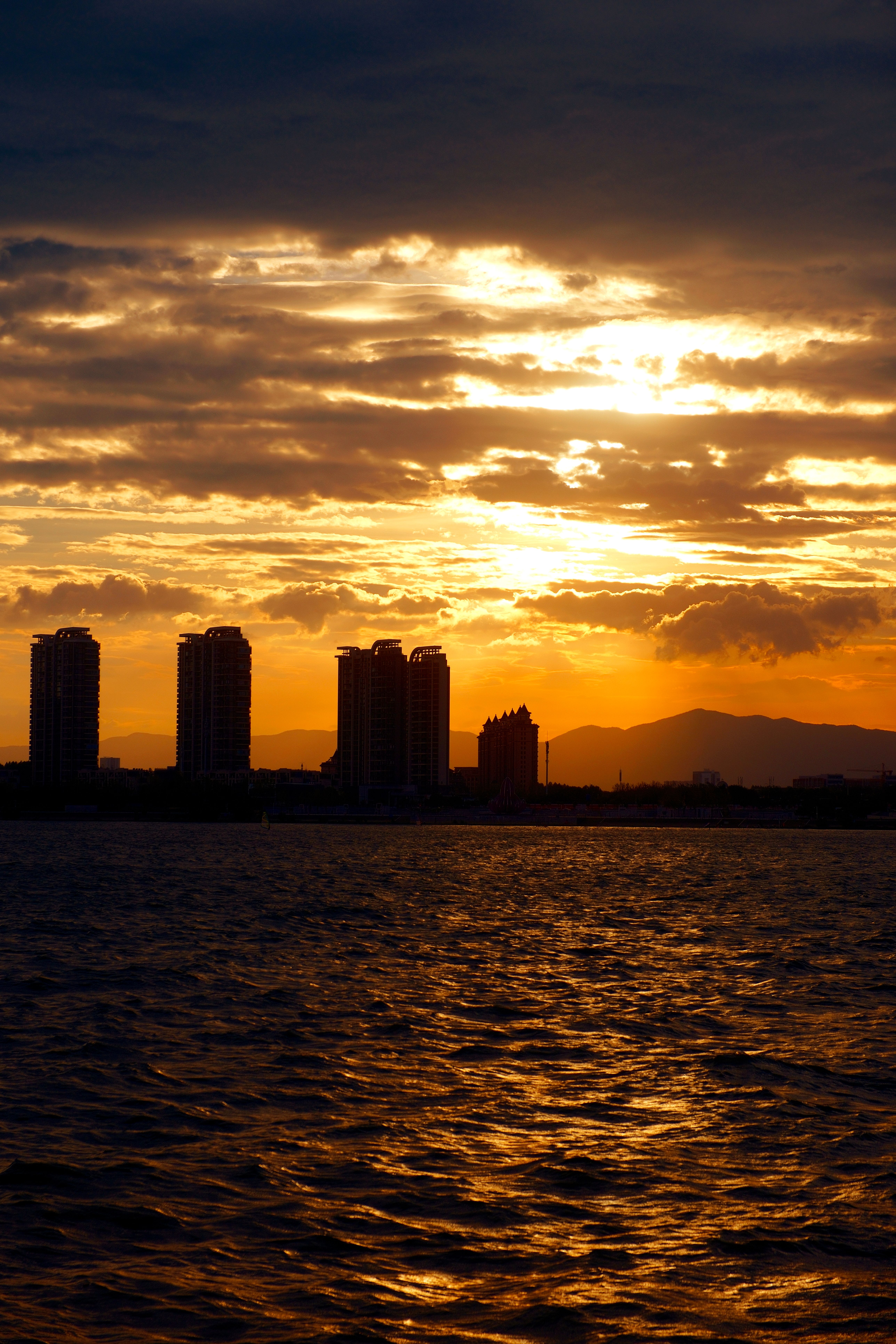 A sunset over the ocean with buildings in the background · Free Stock Photo