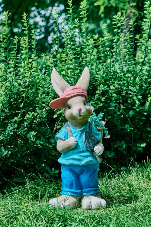 Free Adorable rabbit statue in garden holding tiny flowers, perfect whimsical decor. Stock Photo