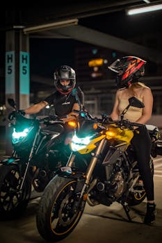 Two motorcyclists wearing helmets on sleek motorbikes during nighttime in urban setting.