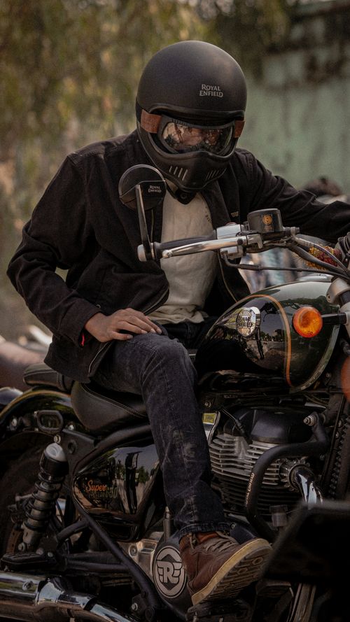 Free A biker in a helmet and black jacket rides a Royal Enfield motorcycle on a sunny day. Stock Photo